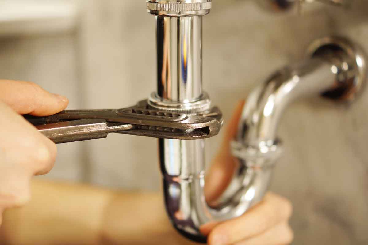 Plumbing repair service. Professional installer with spanner checking pipe.